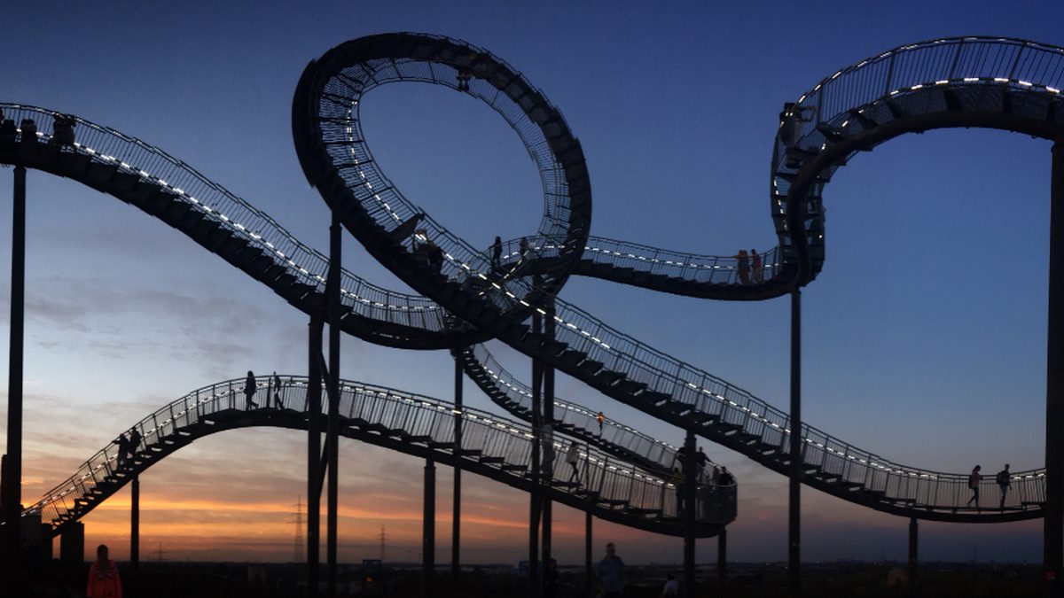 Silhouetted roller coaster loops against an orange and blue sunset sky