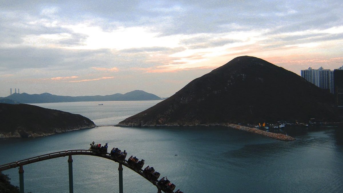 A roller coaster track curving above water with hills in the distance at dusk