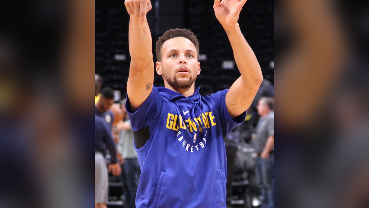 Stephen Curry in a Golden State Warriors warmup shirt following through on a jump shot before a game