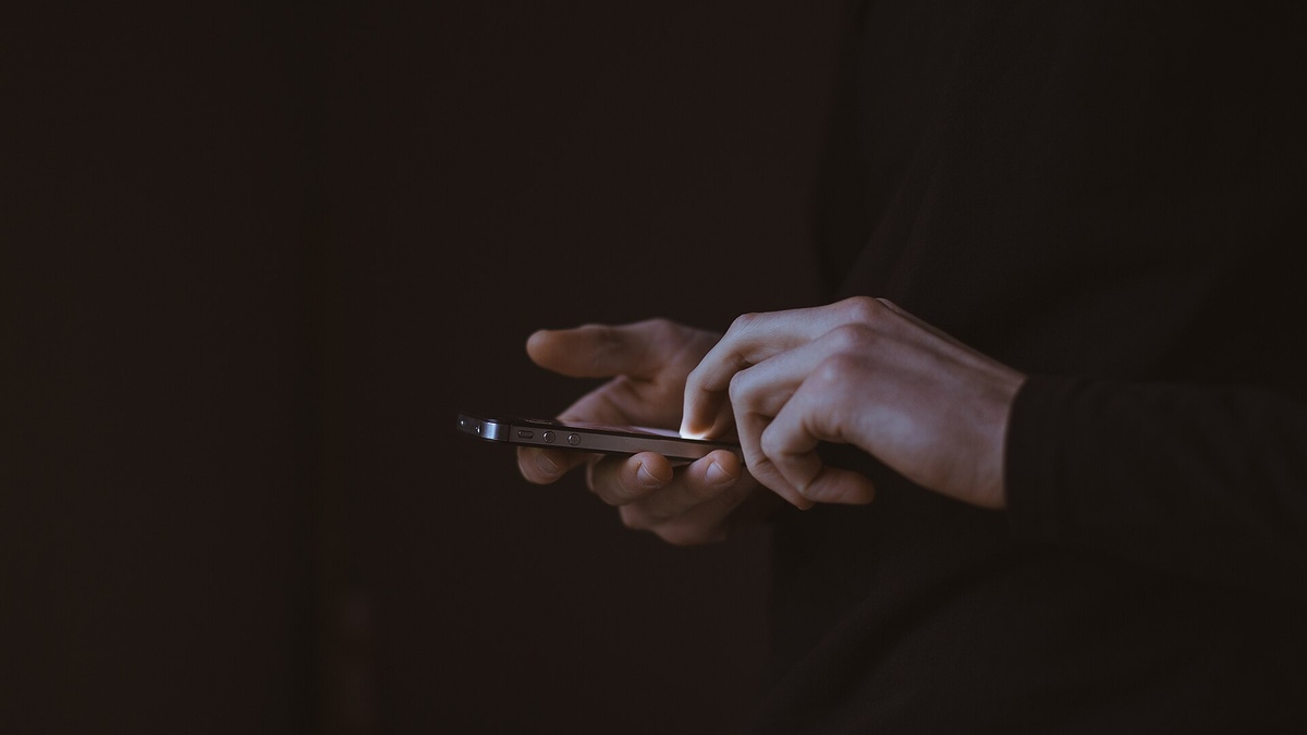 A person's hands typing on a smartphone in a dark room