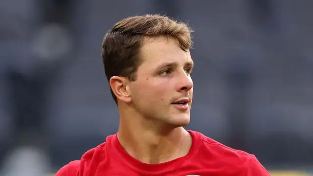 49ers quarterback Brock Purdy in a red 49ers warmup shirt holds a football before a preseason game in 2026