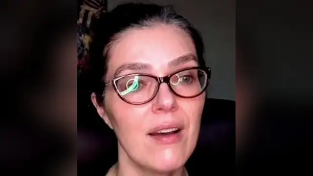 Adrianne Curry in red glasses and a black top talking on a livestream