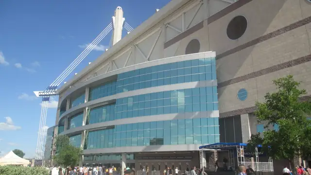 The glass front and white towers of the Alamodome in San Antonio on a sunny day with people walking outside