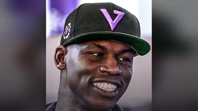 Al Harrington smiling in a black cap with a purple V logo