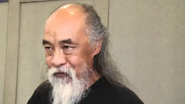 Al Leong with a long white beard and gray hair in a black shirt during an interview
