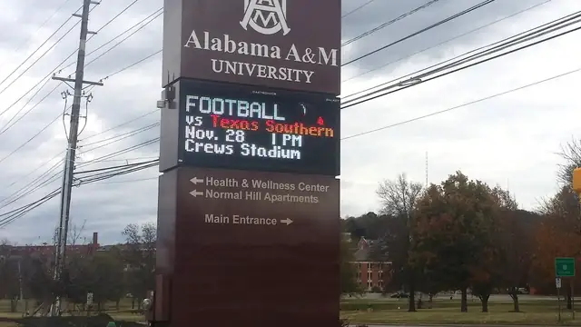 Alabama A&M University entrance sign with a football game notice standing beside a road under a cloudy sky