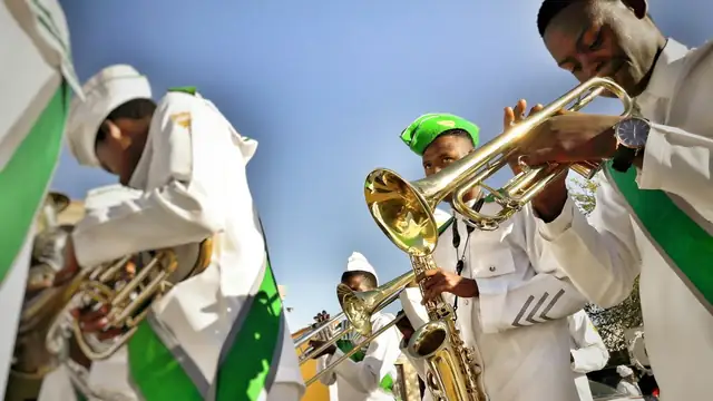 Young Black musicians in white band uniforms with green sashes playing trumpets and horns outdoors