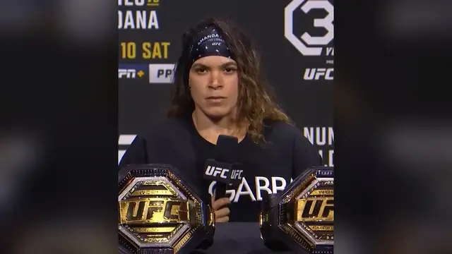 Amanda Nunes sits behind two UFC championship belts at a press conference in 2023