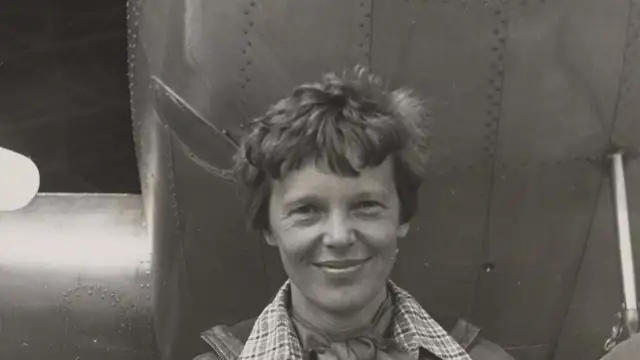 Amelia Earhart smiles while standing beneath the nose of her Lockheed Electra airplane in 1937