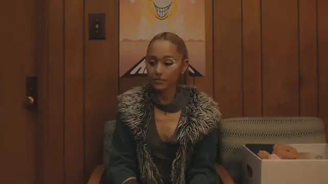 Ariana Grande with slicked-back hair in a fur-trimmed coat in a wood-paneled room