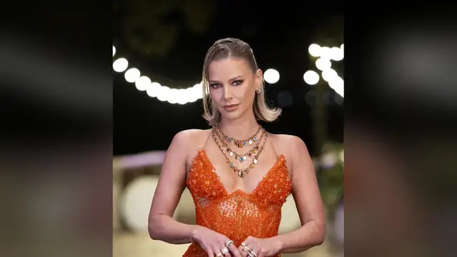 Ariana Madix in an orange beaded dress and layered necklaces posing under string lights