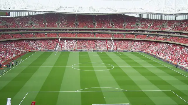 Wide view of the Emirates Stadium pitch and packed red seating under a white curved roof