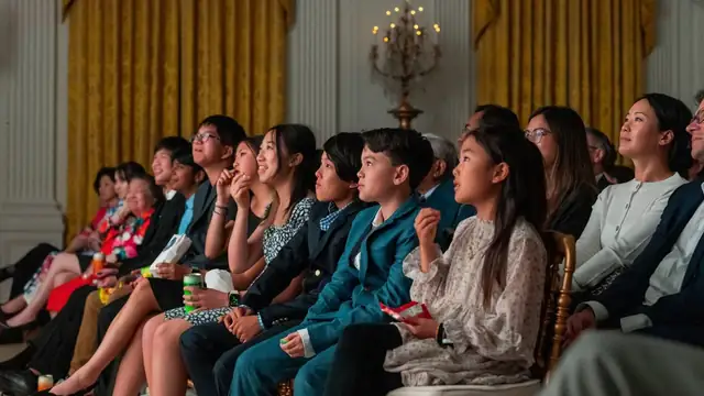 Asian American guests seated in the East Room of the White House listen and smile during a heritage month event