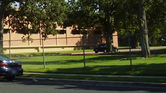 Parked cars along a fenced green lawn and brick building at Huston-Tillotson University in Austin