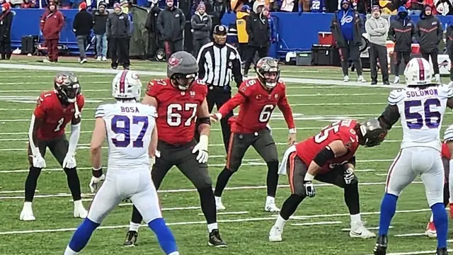 Buccaneers quarterback Baker Mayfield in a red No. 6 jersey stands behind his offensive line before a snap