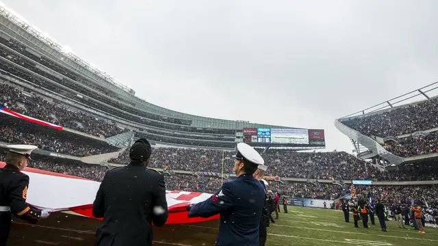 Service members unfurl a giant American flag on the field at Soldier Field as fans fill the stands before a Chicago Bears home game