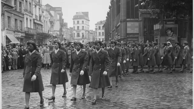 Women of the 6888th Central Postal Directory Battalion march in uniform through a crowded town square in France in 1945