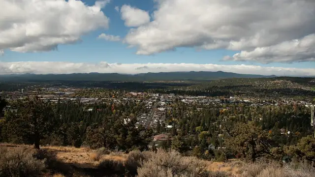 A view over Bend Oregon and its pine-covered neighborhoods from Pilot Butte under puffy white clouds