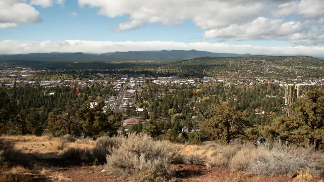 View over Bend Oregon with pine trees and homes below distant mountains under white clouds
