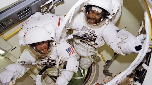 Astronauts Bernard Harris and Michael Foale in white spacesuits preparing to leave the airlock of a space shuttle