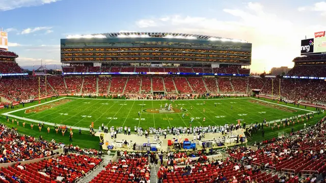 A packed NFL stadium at sunset with fans filling the stands around a bright green field