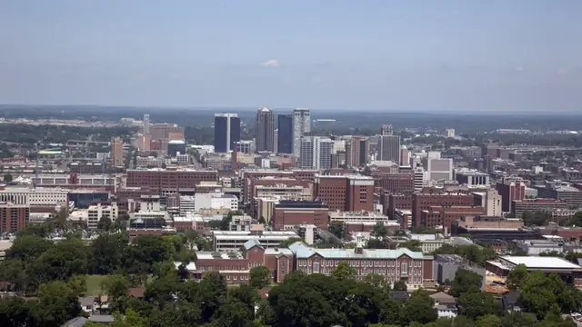 Downtown Birmingham, Alabama, skyline rising above tree-lined neighborhoods under a pale blue sky