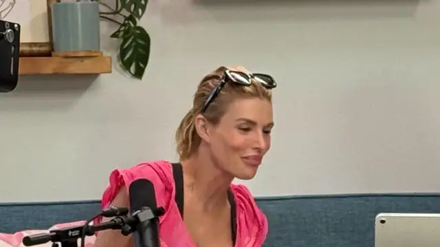 Brandi Glanville in a pink top smiling during a podcast taping