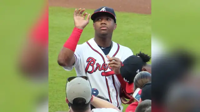 Ronald Acuña Jr. in a white Atlanta Braves jersey and cap waving to fans