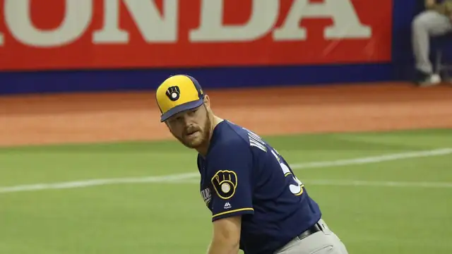Milwaukee Brewers pitcher Brandon Woodruff in a navy jersey and ball-and-glove cap looking over his shoulder to check a runner
