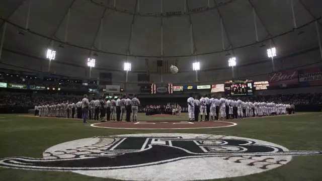 Players lined up along the baselines on the infield under the white dome roof of Tropicana Field before a baseball game