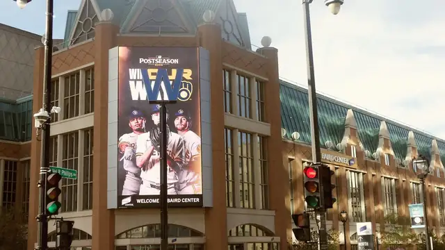 A tall video screen on a Milwaukee convention center shows Brewers players under a Win Our Way postseason banner