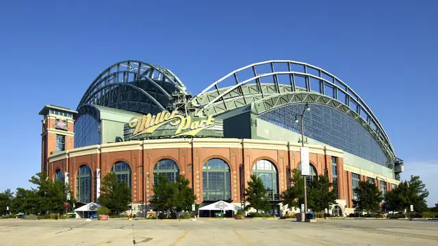 The brick and glass home ballpark of the Milwaukee Brewers with its fan-shaped arched roof under a clear blue sky, shown when it still carried its former Miller Park name