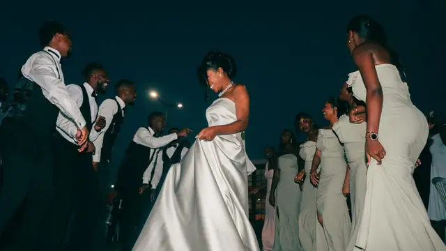 A bride in a white gown dancing with bridesmaids and groomsmen at a nighttime wedding party