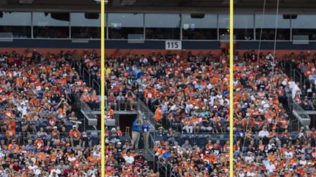 A packed crowd of Broncos fans in orange fills the stands behind the yellow goalposts at the stadium in Denver