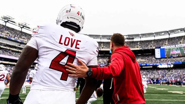 Cardinals running back Jeremiyah Love seen from behind in a white No. 4 jersey as a coach in a red hoodie pats his back
