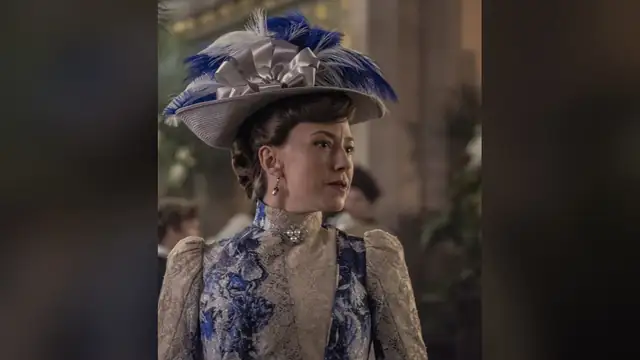 Carrie Coon in a blue feathered hat and a blue lace gown as Bertha Russell in The Gilded Age
