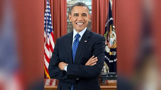 Barack Obama smiling with arms crossed in the Oval Office