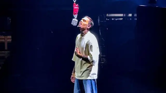 Chris Brown singing on a dark stage beneath a hanging crystal microphone
