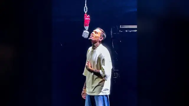 Chris Brown singing on a dark stage beneath a hanging microphone