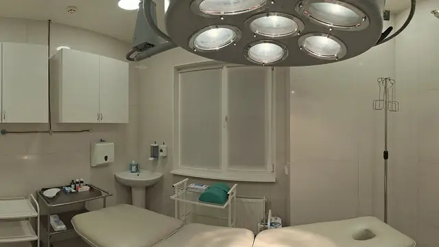 An empty treatment room with a padded table under a surgical light