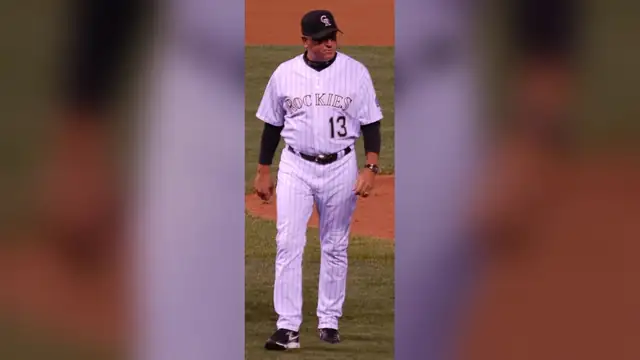 Clint Hurdle walking across the field in a white pinstriped Colorado Rockies No. 13 uniform and black cap