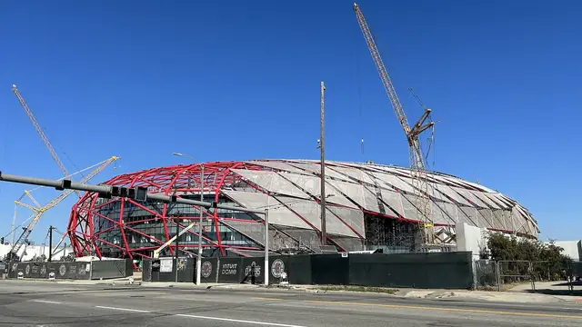 The Intuit Dome arena rises above a construction site under a blue Southern California sky