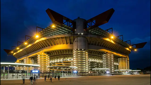 San Siro stadium towers lit at dusk with red steel beams above the spiral ramps in Milan