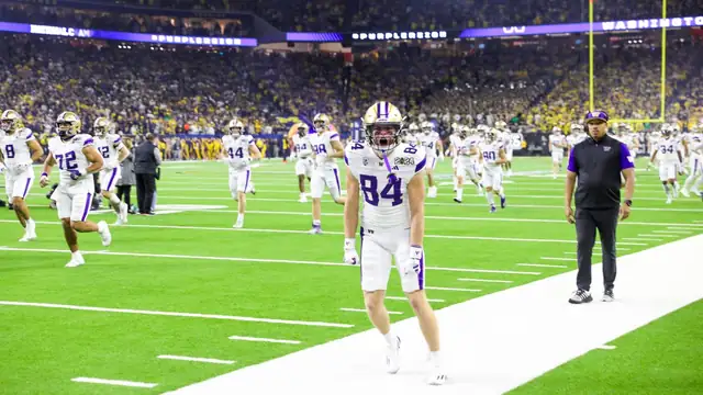 Washington players in white uniforms warm up on the field before the 2024 College Football Playoff national championship game in Houston