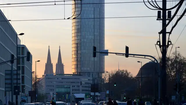 Cologne Cathedral spires and a glass tower at dusk above a busy Cologne street