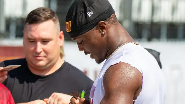 Terry McLaurin in a Commanders cap signs autographs for fans at training camp in 2024