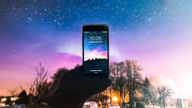 A hand holding up a lit smartphone against a starry night sky