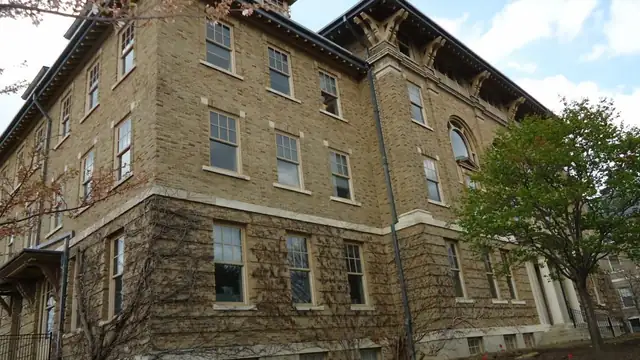 A brick and stone hall with ivy beside a leafy tree on the Cornell University campus