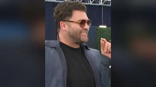 CT Tamburello grinning in aviator sunglasses and a gray jacket on a red carpet