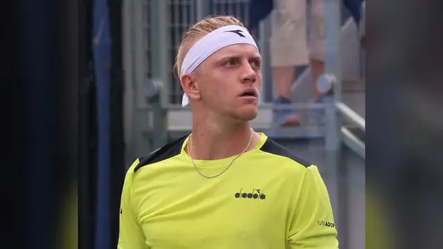 Alejandro Davidovich Fokina in a lime green shirt and white headband looks up while walking on a hard court